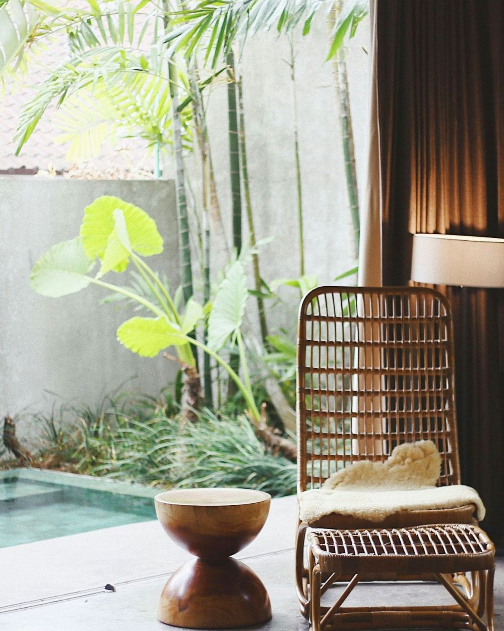 Bright living room with a rattan chair next to a small pool and tropical garden